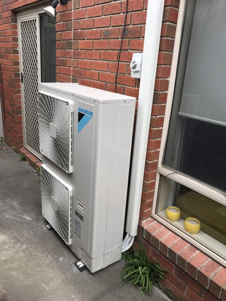Daikin split system air conditioning outdoor unit installed against a brick wall